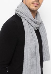 Harmaa ribbikuvioinen neulehuivi kaulalla, valmistettu pehmeästä materiaalista, jossa on hieno kiilto, yhdistettynä mustaan villapaitaan.