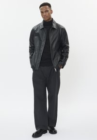 Black leather jacket with a zip front and quilted detailing, paired with a black turtleneck and loose-fitting black trousers. Black shoes.