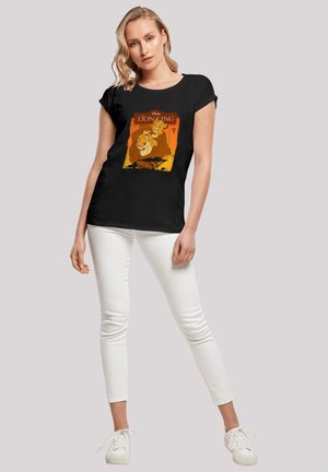 Black t-shirt featuring a colorful "Lion King" graphic, short sleeves, relaxed fit, and made of soft cotton fabric. Model wearing white pants.