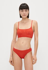 Conjunto de lencería roja que incluye un bralette con patrón y tirantes finos, además de braguitas estilo bikini a juego. Tejido suave con una textura lisa.