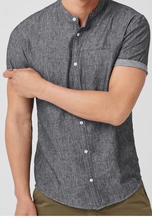 Uomo che indossa una camicia grigio scuro a maniche corte con bottoni e colletto alla coreana, arrotolando una manica mentre incrocia le braccia.