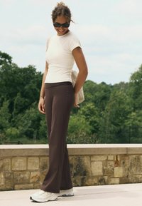 Hnedé rozšírené nohavice skombinované s priliehavým bielym topom a bielymi teniskami. Outfity majú ležérny štýl s jemnou ryhovanou textúrou.