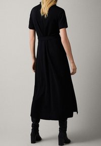 Sort, kortærmet kjole med taljeret liv, blød nederdel og sideslidser. Lavet af glat stof, har et minimalistisk design.