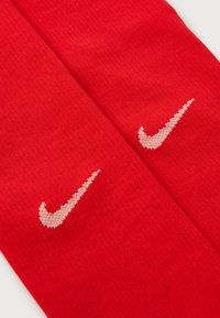 Punased Nike sokid kontrastse beeži tikitud swoosh logo'ga, tiheda kootud tekstuuri ja katkematu kujundusega.