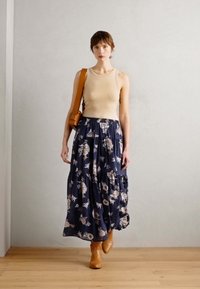 Beige tank topp, marineblomstrete maxiskjørt med lagdelt design, kombinert med brune ankelstøvler og en brun crossover-veske. En enkel, avslappet silhuett.
