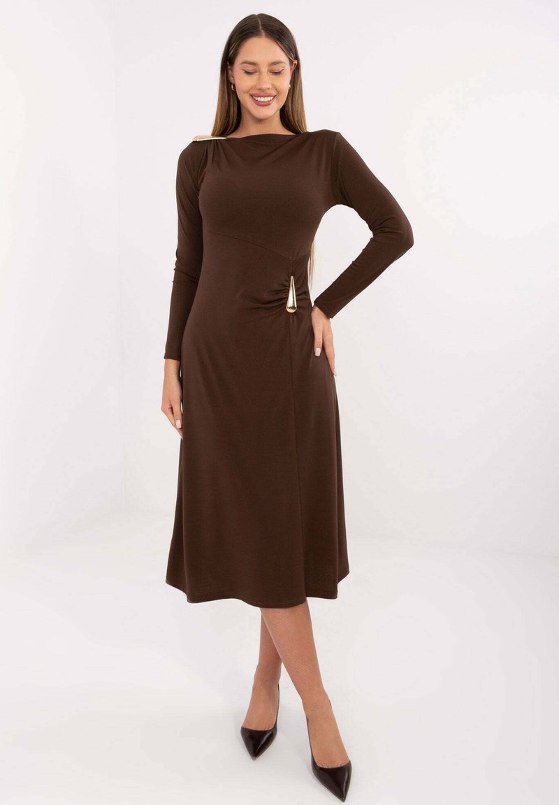 Brązowa sukienka z długim rękawem, dopasowaną górą, płynną spódnicą oraz złotym akcentem na lewym ramieniu i talii. Gładka tekstura.