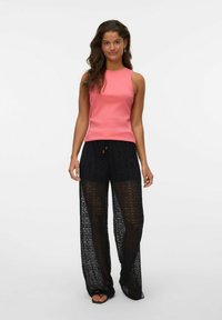 Top senza maniche rosa con texture a coste abbinato a pantaloni in pizzo nero trasparente caratterizzati da gamba larga e intricati motivi circolari.