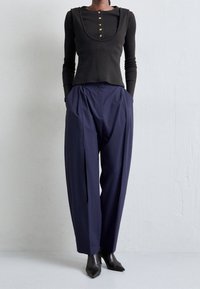 Schwarzes Langarmoberteil mit U-Ausschnitt und goldenen Knöpfen, kombiniert mit lockeren navy Hosen, die seitliche Taschen und eine strukturierte Oberfläche haben.