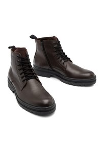 Brązowe skórzane botki za kostkę o gładkiej fakturze, z wiązaniem z przodu, bocznym zamkiem błyskawicznym i teksturowaną gumową podeszwą zapewniającą przyczepność.