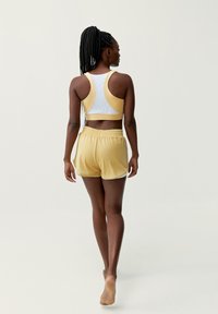 Conjunto deportivo que incluye un sujetador deportivo blanco y amarillo con diseño de espalda nadadora y pantalones cortos amarillos a juego con cinturilla elástica.