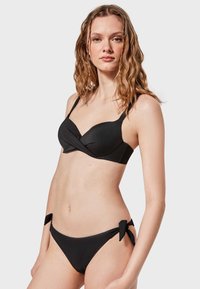Conjunto de bikini negro que presenta un diseño trenzado en la parte superior con tirantes ajustables, y braguitas a juego con lazos en los laterales.