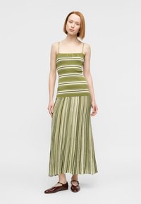 Μάξι φόρεμα με πράσινες ρίγες και λεπτές τιράντες, με εφαρμοστό μπούστο και ροής πλισέ φούστα, συνδυασμένο με καφέ επίπεδα παπούτσια.