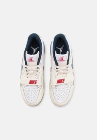Paire de baskets blanches Nike avec un logo rouge et une doublure intérieure noire, vues de dessus sur un fond clair uni.
