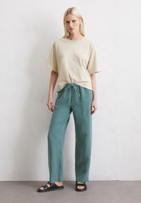 Beige t-shirt met korte mouwen en losse teal broek met trekkoord. Platte zwarte sandalen maken de outfit compleet. Eenvoudig, ontspannen ontwerp.