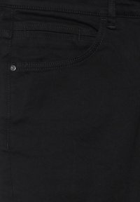 Zwarte denim jeans met een voorzak waarbij de stiksels zichtbaar zijn en een kleine metalen knop. De stof heeft een lichte textuur.
