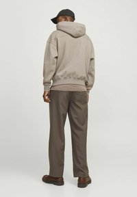 Light beige hoodie with a large back hood, paired with dark brown wide-leg trousers and brown shoes. The fabric appears soft and casual.