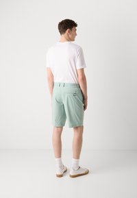 Lysegrønne shorts lavet af stof, med to baglommer og et logo. Kombinationen med en hvid t-shirt og hvide sneakers.