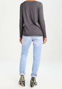 Gray long-sleeve top with scalloped lace hem, paired with light blue rolled-up jeans and floral heels featuring black, green, and beige patterns.