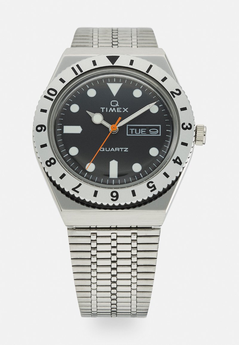 Montre-bracelet à quartz avec un cadran noir, un boîtier en acier inoxydable et un bracelet en maille métallique. Équipée de marqueurs d'heure blancs, d'une trotteuse orange et d'un affichage jour-date.