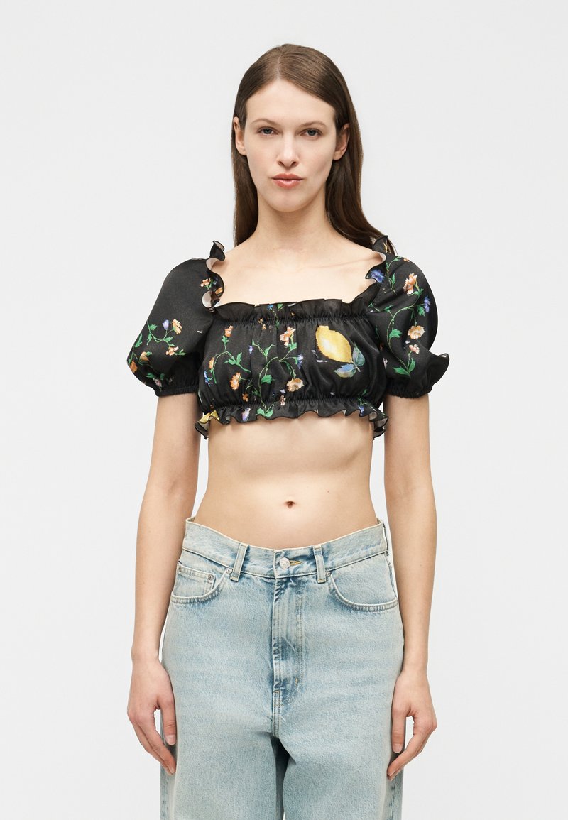 Γυναίκα που φοράει μαύρο κοντό μπλουζάκι με floral και πεταλούδες μοτίβα και φουσκωτά μανίκια, σε συνδυασμό με ανοιχτό μπλε ψηλόμεσα τζιν.