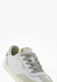Białe skórzane sneakersy z szarymi zamszowymi akcentami, złotą zakładką na pięcie, szarymi sznurówkami i perforowanymi detalami po bokach. Teksturowana gumowa podeszwa.