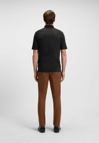 Svart kortärmad polo med rak fåll och klassisk krage, kombinerad med bruna slim-fit byxor och svarta skor.