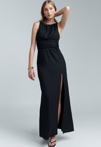 Schwarzes Maxikleid aus einem subtil strukturierten Stoff, ärmelloses Design, geraffter Ausschnitt, geraffte Taille und hoher Schlitz bis zum Oberschenkel.