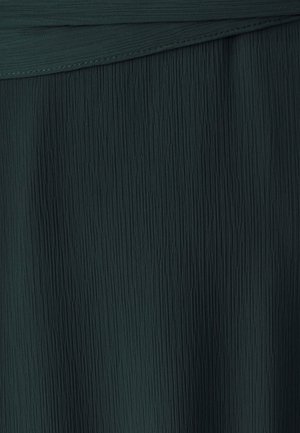 Tamnozeleni teksturirani materijal s vertikalnim nabranjem, stvarajući valoviti izgled s glatkim završetkom na gornjem rubu.