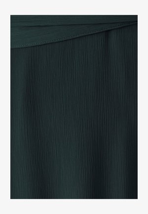 Mørkegrøn tekstureret stof med lodrette plisseringer, der skaber et bølget udseende med en glat finish ved den øverste kant.