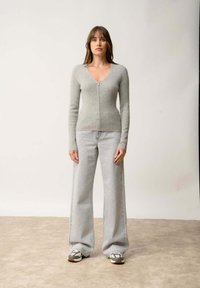 Hellgrauer Zip-Front-Pullover mit langen Ärmeln, gerippter Textur, kombiniert mit hochgeräumten hellblauen weiten Jeans und mehrfarbigen Sneakers.