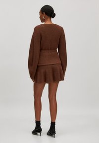 Bruine gebreide trui met oversized mouwen en een strikdetail in de taille, gecombineerd met een bijpassende flared rok; gladde textuur, nauwsluitend in de taille.