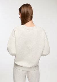 Felpa oversized grigia chiara con scollatura rotonda, spalle basse e polsini a costine. Tessuto morbido, progettato per il comfort.