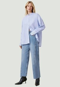 Ljust blå randig skjorta med knappar och långa ärmar, matchad med löst sittande ljus denimjeans och svarta ankelstövlar.