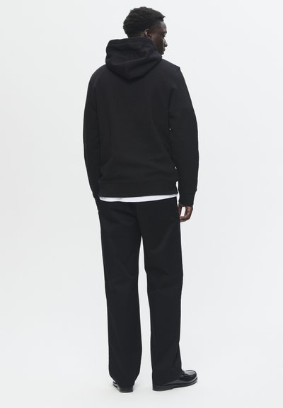 Haut à capuche noir avec cordon de serrage, associé à un pantalon noir. Texture lisse, design ajusté et style minimaliste sans marque visible.
