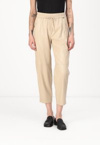Beige, cropped nep leren broek met een elastische tailleband en trekkoord, voorzien van zijzakken en een gladde, glanzende textuur.