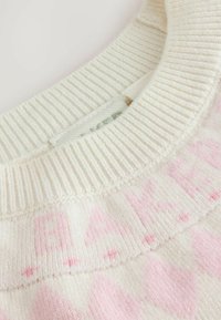 Suéter de punto en color crema con cuello de textura acanalada y sutiles letras y patrones en rosa sobre un tejido suave.