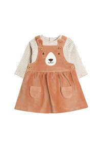 Vestido de pana marrón para niña pequeña con cara de oso y orejas, llevado sobre una camisa de manga larga a rayas beige y blanca. Tiene dos bolsillos en la parte frontal del vestido.