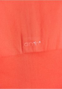 Korallivärvi kangas, millel on sile tekstuur. Omab tooni logo "aimn®", mis on embosseeritud alumise ribatud osa kohale.