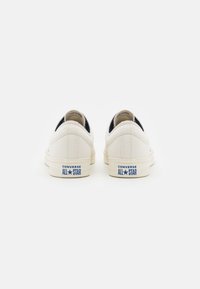 Bílé plátěné tenisky s nízkým střihem, na patě s modrým logem "Converse All Star" a texturovanou gumovou podrážkou.