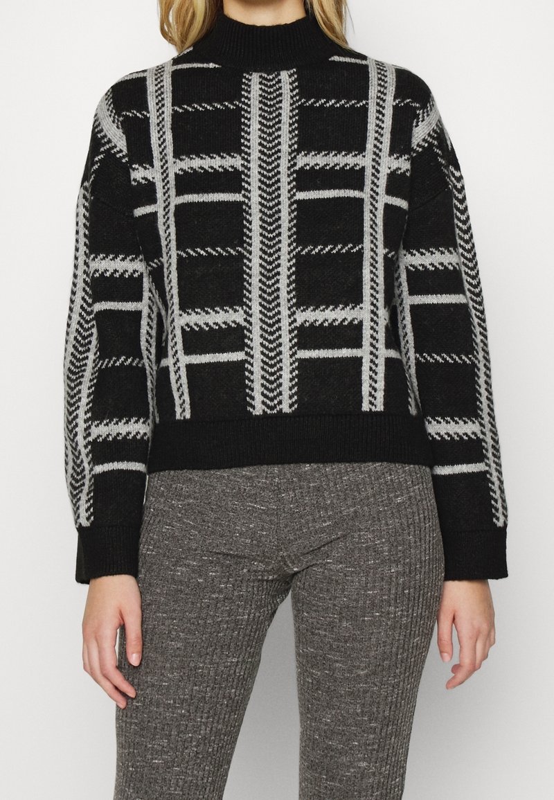 Czarny i szary sweter w wzory z wysokim ściągaczem przy dekolcie, wyróżniający się geometrycznym wzorem, miękką teksturą i lekko luźnym krojem.