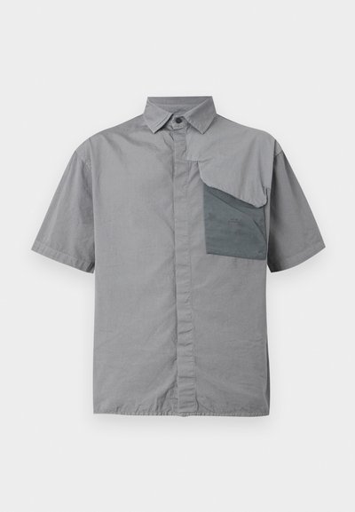 Camisa de manga curta em tecido cinza claro, com um bolso de remendo no lado esquerdo do peito, apresentando uma aba dobrada, e com fecho de botões na frente.