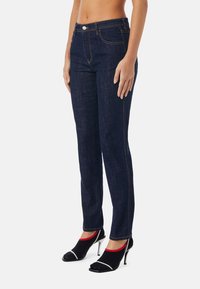 Tmavé džíny s úzkým střihem, designem pěti kapes, kontrastním prošitím a středním pasem. Vytvořené s černými a červenými ponožkovými lodičkami.