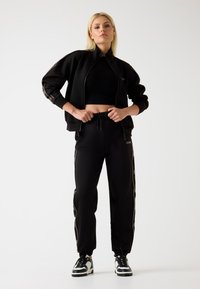 Czarny, sportowy dres składający się z kurtki na zamek i spodni z bokami. Zawiera krótki top oraz sportowe czarno-białe sneakersy.