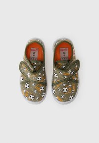 Chaussons en tissu vert avec un motif de ballon de football et d'équipement, semelle grise, sangle velcro et doublure orange. Présente des éléments de design ludiques.
