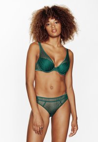 Ensemble de lingerie verte en tissu mesh. Le soutien-gorge présente une bonnette lisse et des bretelles larges ; le bikini a une taille basse avec un bord contrastant.