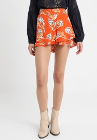 Spódnica w pomarańczowy kwiatowy wzór z falbaną na dole, wykonana z lekkiego materiału. Noszona z czarną bluzką z długim rękawem i beżowymi botkami za kostkę.