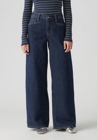 Jeans en denim foncé à taille haute et jambes larges, avec couture visible, poches avant et fermeture par bouton classique.