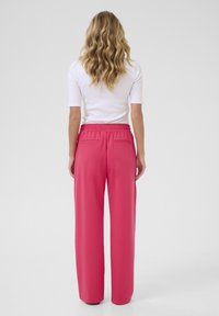 Pantalons larges roses avec une taille élastique et deux poches arrière, fabriqués à partir d'un tissu lisse, vus de dos.