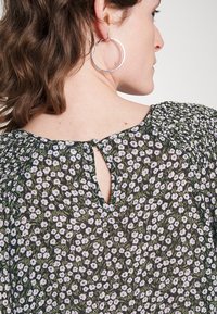 Blusa floral em tecido escuro com flores roxas e brancas, apresentando um decote em gota nas costas e detalhes franzidos nos ombros.