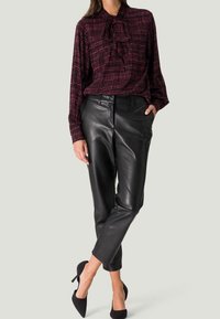 Blouse bordeaux à motifs avec un nœud, associée à un pantalon en cuir noir et des talons hauts noirs. Texture lisse et coupe décontractée.